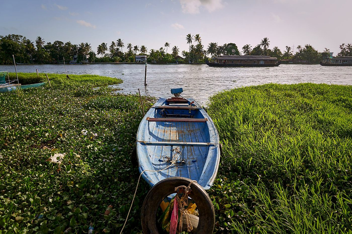 A small boat at the water's edge with houseboats passing in the distance